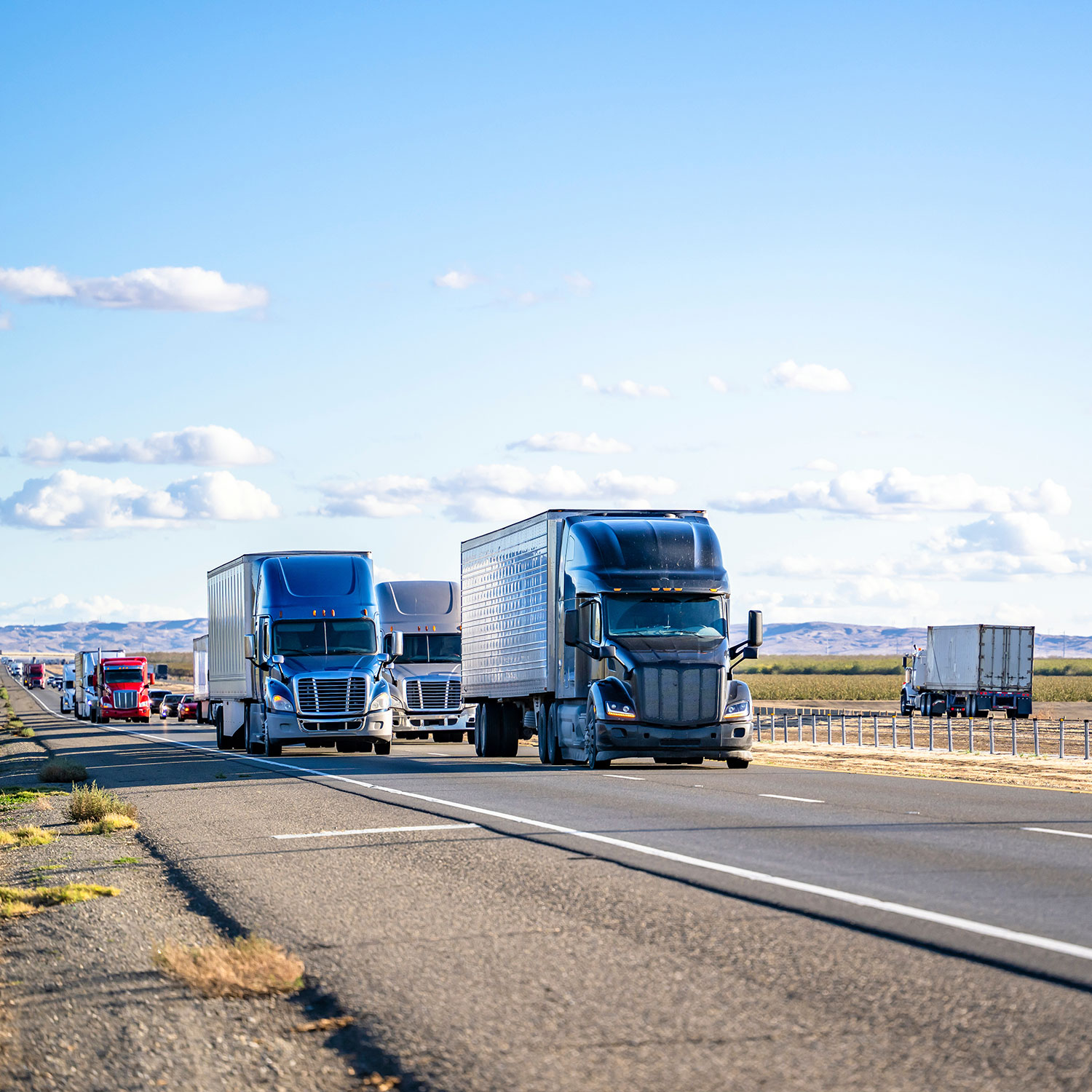 Convoy of the different big rigs semi trucks carry cargo in semi trailers running on a divided highway road.